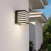Modern outdoor wall light fixture on a house exterior with a clear sky.