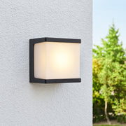 Outdoor wall light fixture on a textured wall with blurred greenery in the background