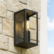 Black outdoor wall light fixture on a stone wall with clear sky background