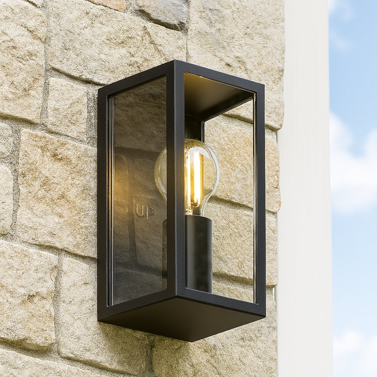 Black outdoor wall light fixture on a stone wall with clear sky background