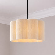 A modern multi-light pendant fixture with a fluted, scalloped drum shade made of textured cream fabric, suspended by a black cord in a minimalist room setting.