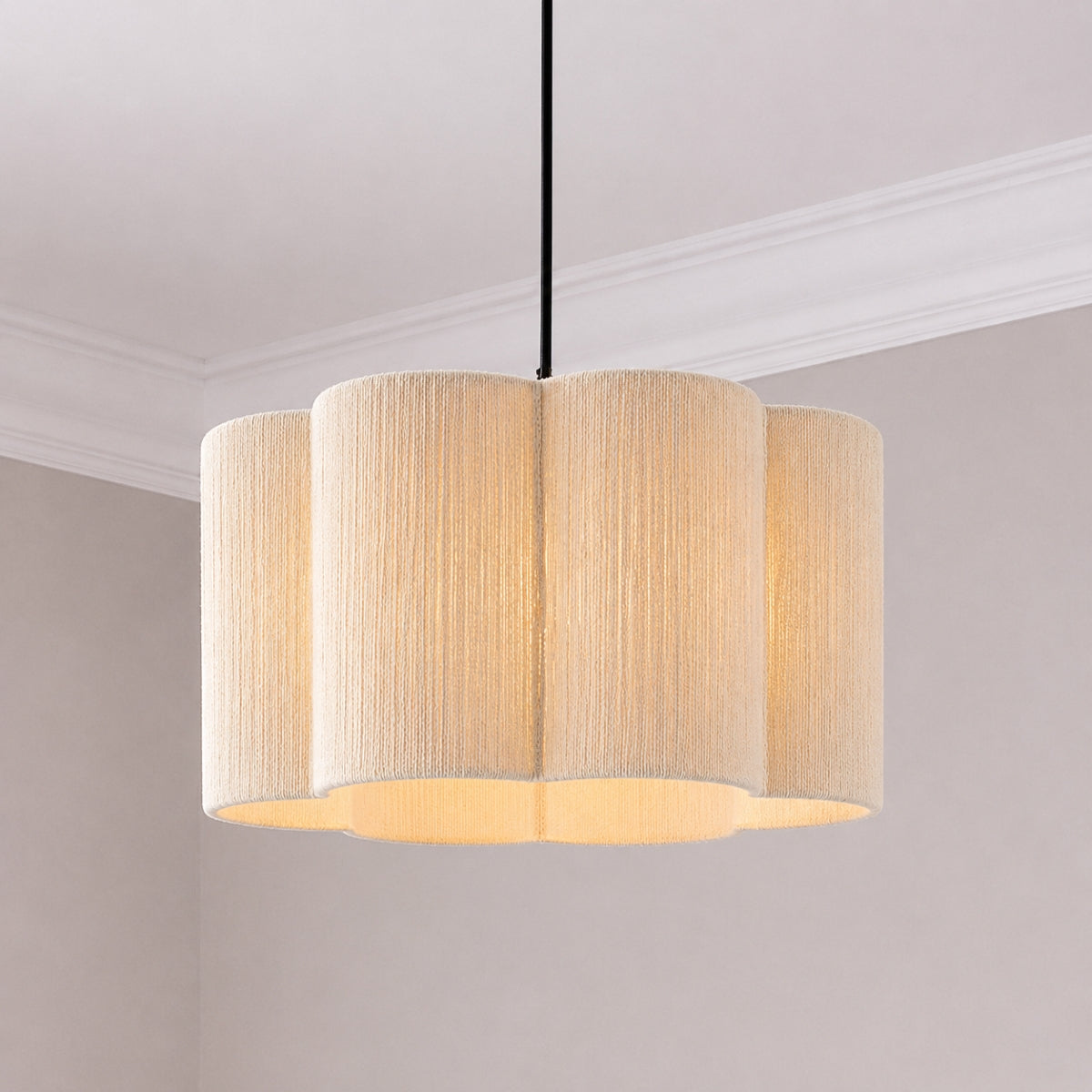 A modern multi-light pendant fixture with a fluted, scalloped drum shade made of textured cream fabric, suspended by a black cord in a minimalist room setting.