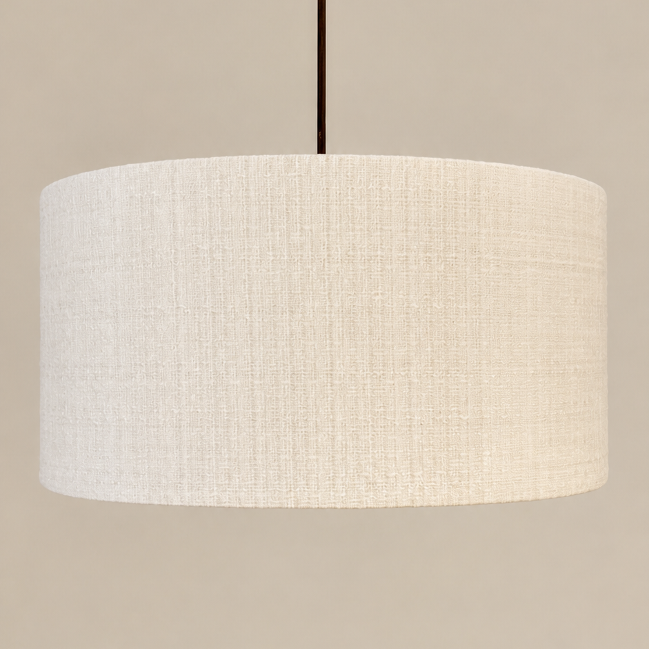 A drum pendant light with a textured off-white linen shade, suspended by a thin dark brown cord against a solid beige background.