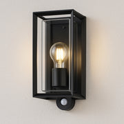 Black outdoor wall light fixture with a bulb on a light gray wall.