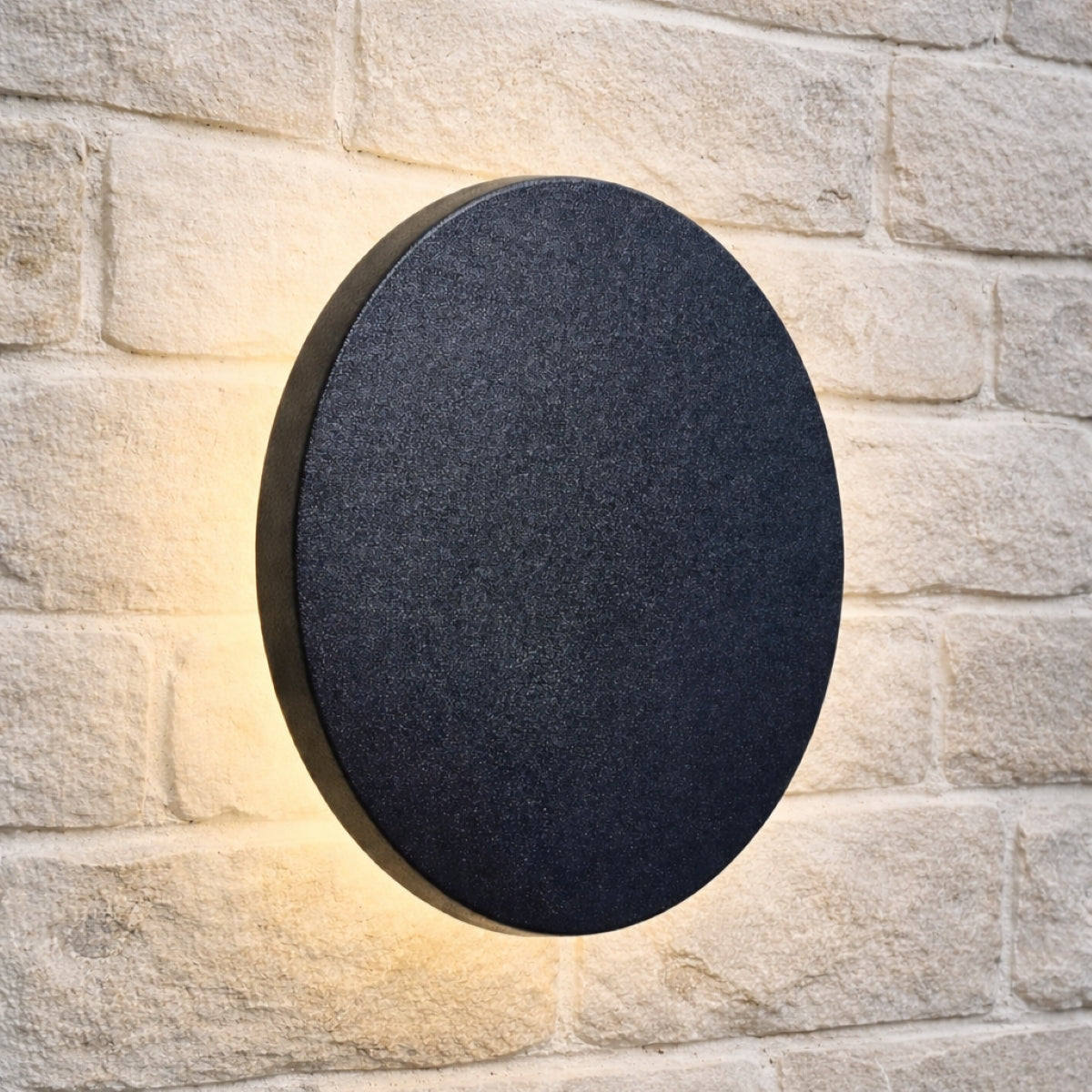 Round black outdoor wall light fixture on a stone wall.