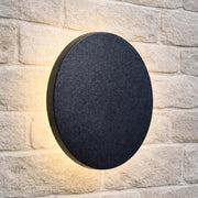 Round black outdoor wall light fixture on a stone wall.