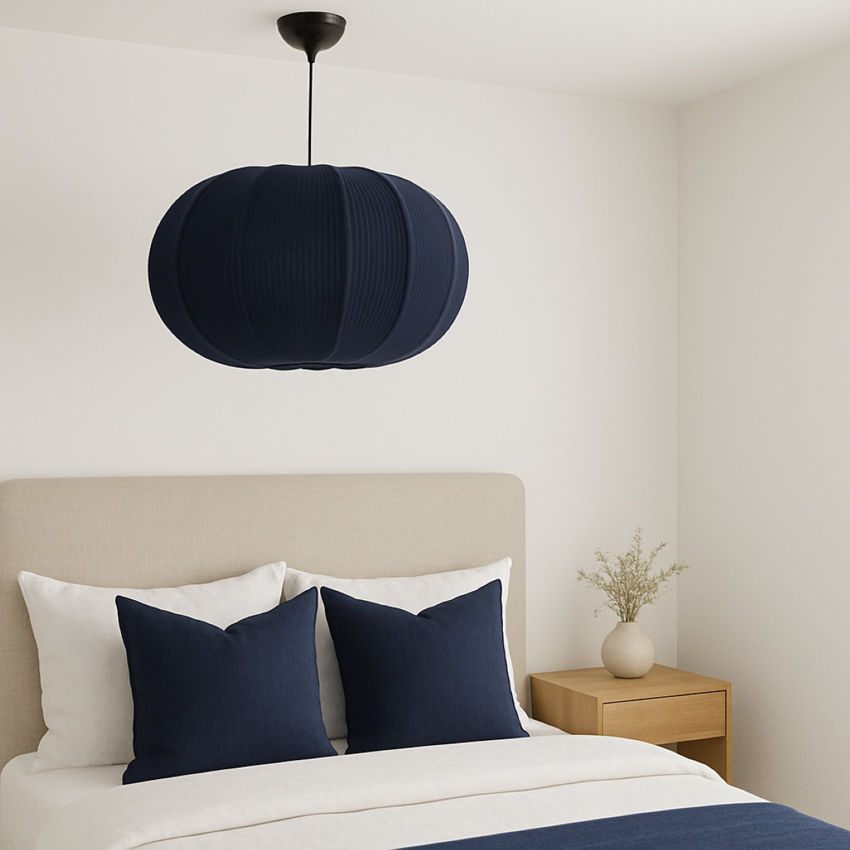 Navy pendant light above a bed with white bedding and navy pillows in a bedroom setting.