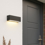 Modern outdoor wall light fixture on a white wall next to a gray door.