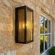 Outdoor wall light fixture on a stone wall with a window in the background
