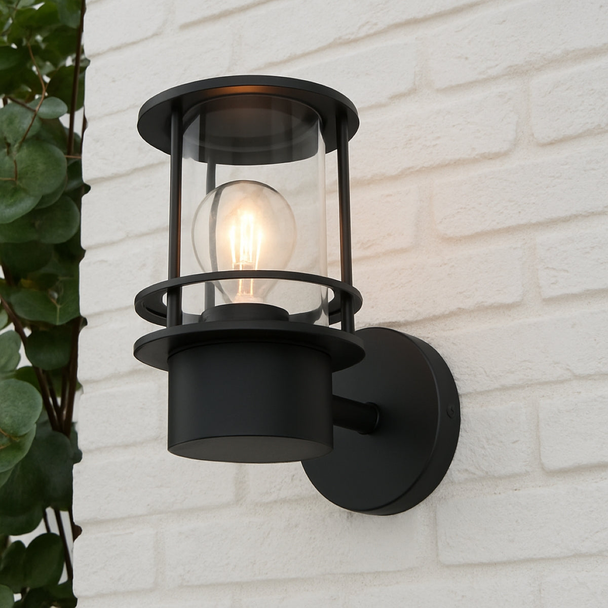 Black outdoor wall light fixture on a white brick wall with a plant to the left.