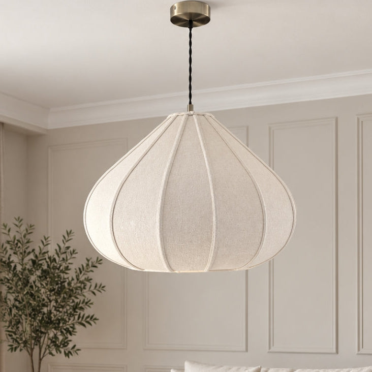 A modern teardrop-shaped pendant light with a textured cream fabric shade hangs in a bright, contemporary living room with a beige sofa, wooden coffee table, and neutral decor.