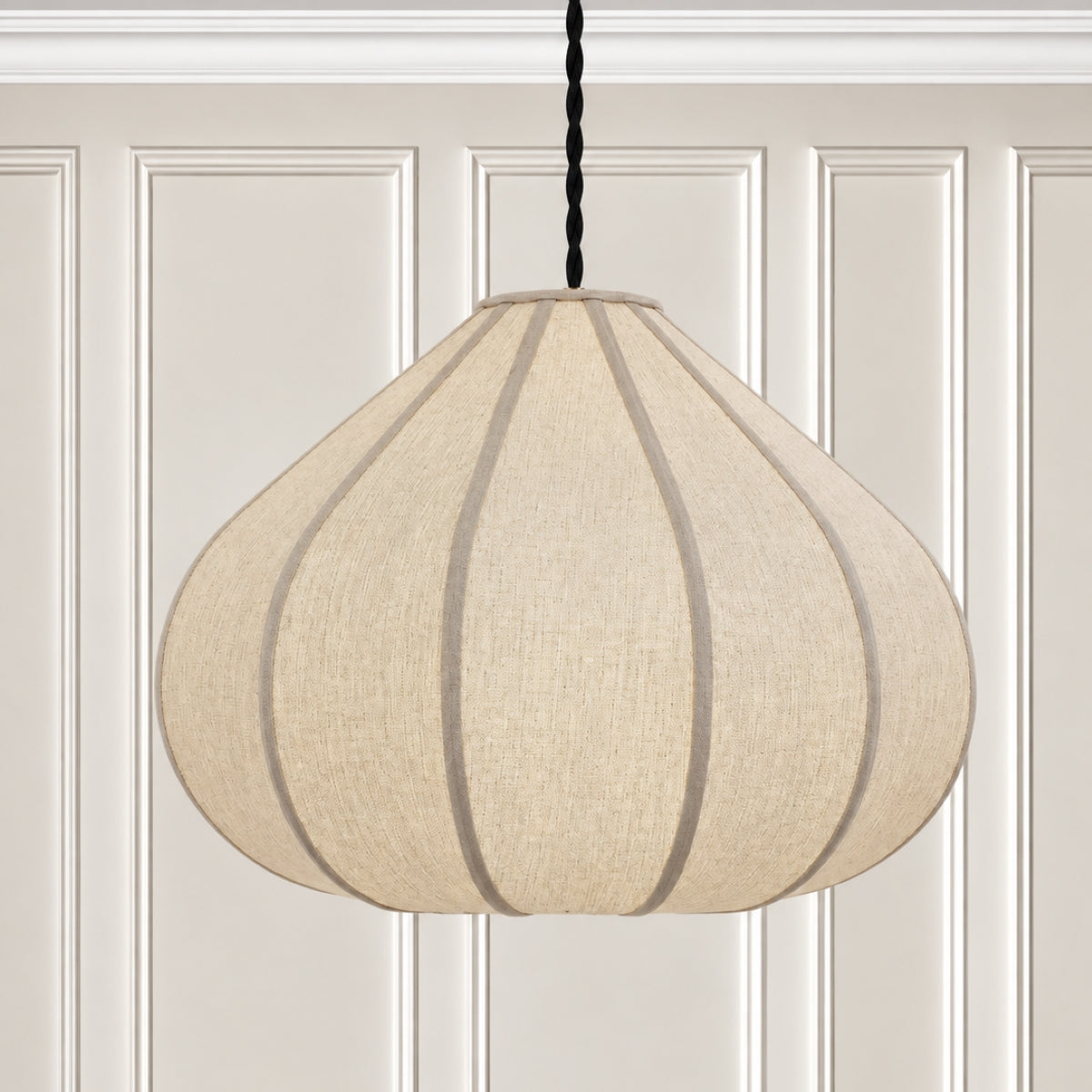 A modern pendant light with a large, teardrop-shaped beige linen shade featuring vertical dark gray pleats, suspended by a black cord against a white paneled wall.
