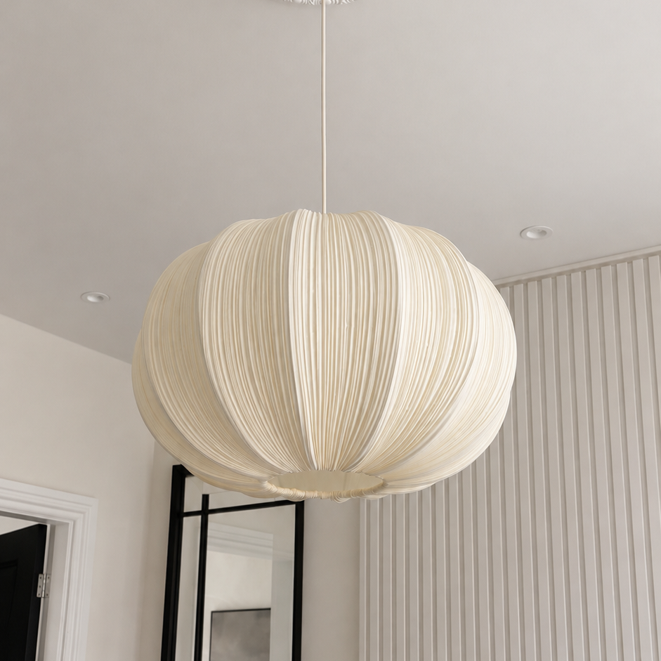 A cream-colored pleated paper pendant light hanging from a decorative ceiling medallion in a modern, minimalist room with white walls and a vertical slatted accent wall.