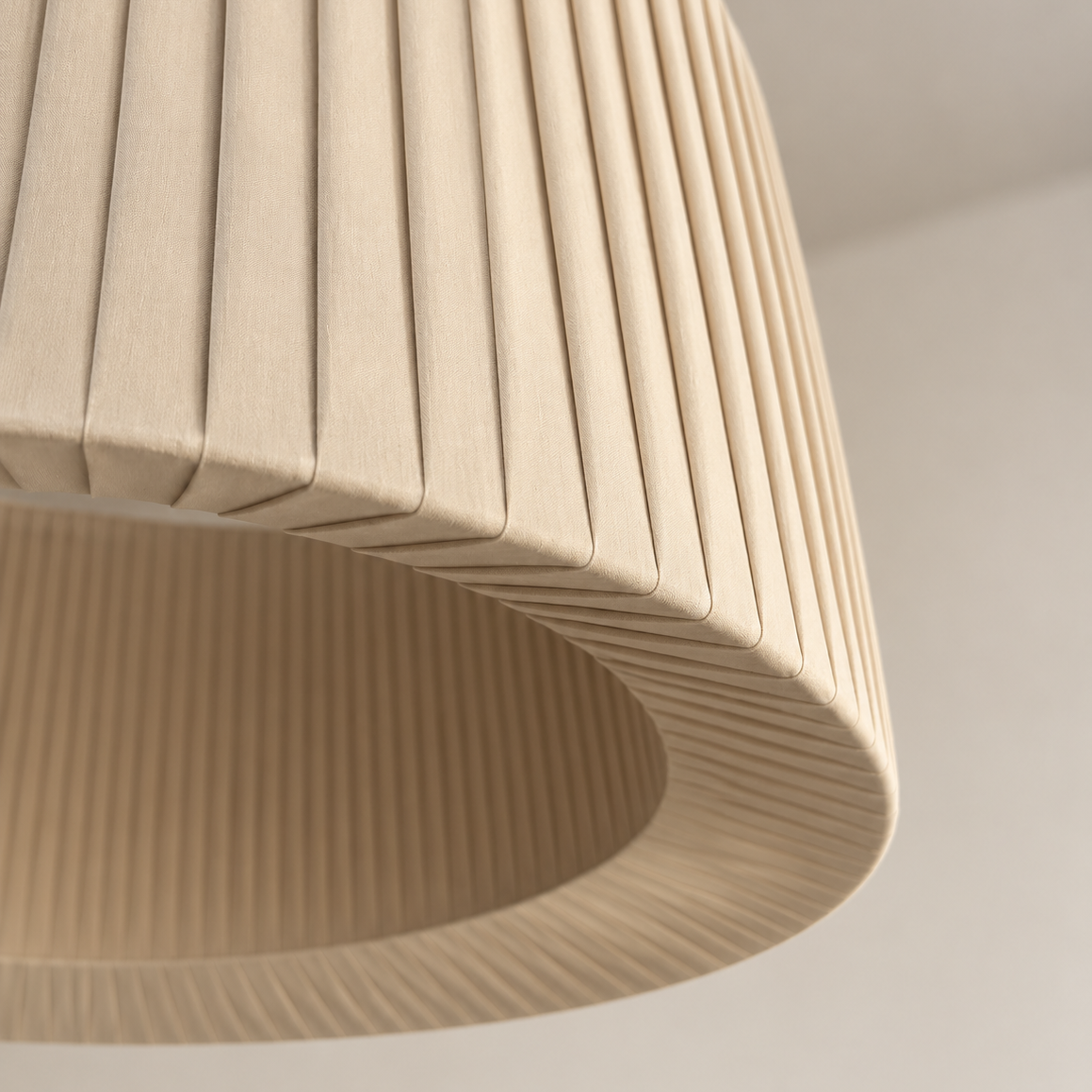 Close-up of a pleated dome-shaped ceiling light fixture in a warm beige fabric, showing the texture and curved underside against a neutral off-white background.