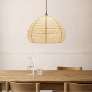 Woven pendant light hanging above a wooden dining table with a neutral wall background.