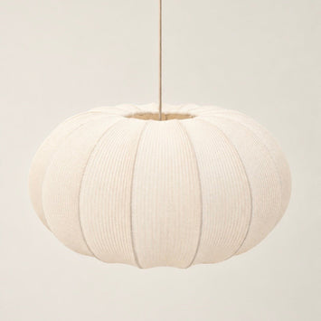 A modern pendant light with a ribbed, pumpkin-shaped white fabric shade and a brushed brass metal canopy and rod, shown hanging against a minimalist off-white wall.