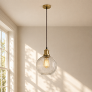 Pendant light with glass shade and gold fixture hanging in a room with sunlight filtering through a window.
