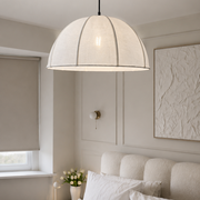 A modern dome-shaped pendant light with a textured off-white fabric shade and a dark metal canopy, hanging in a neutral-toned bedroom above a bed.