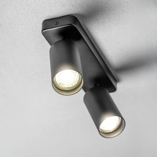 The black Nell twin lamp consists of two cylindrical spotlights, both of which can be tilted and adjusted on their own axis. The spotlights are attached to a rectangular bracket, which makes them equally suitable for mounting on walls and ceilings. Made of an aluminium body and powder coated black, the lamp with its simple design fits well into different spaces.