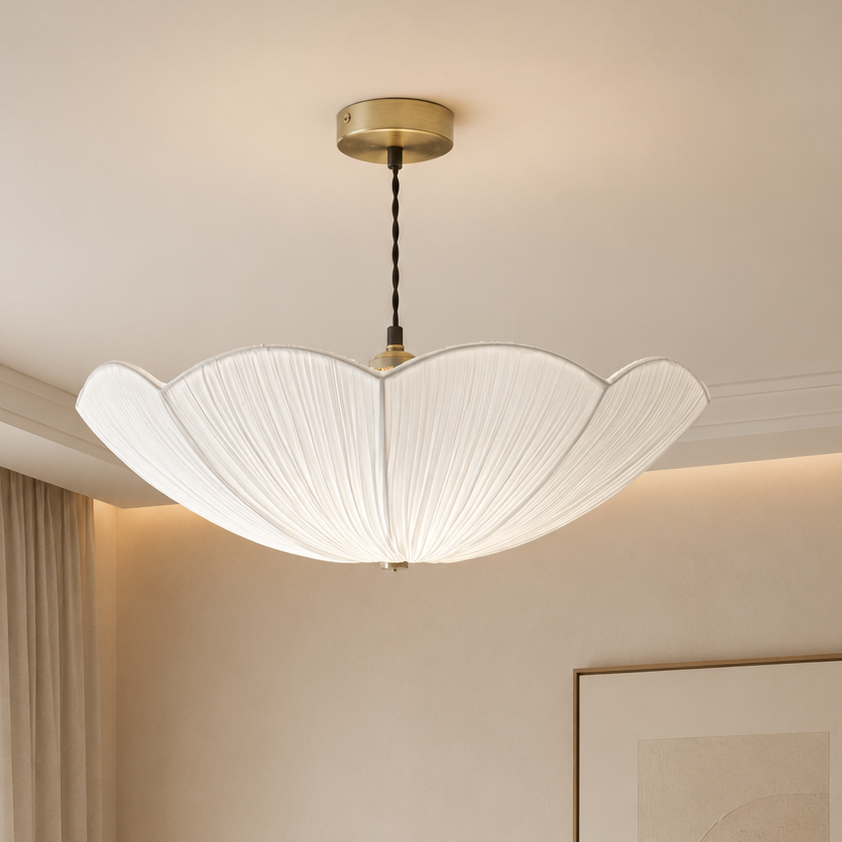 A modern flower-shaped pendant light with a white pleated shade and a gold canopy, hanging in a warm, minimalist beige room.