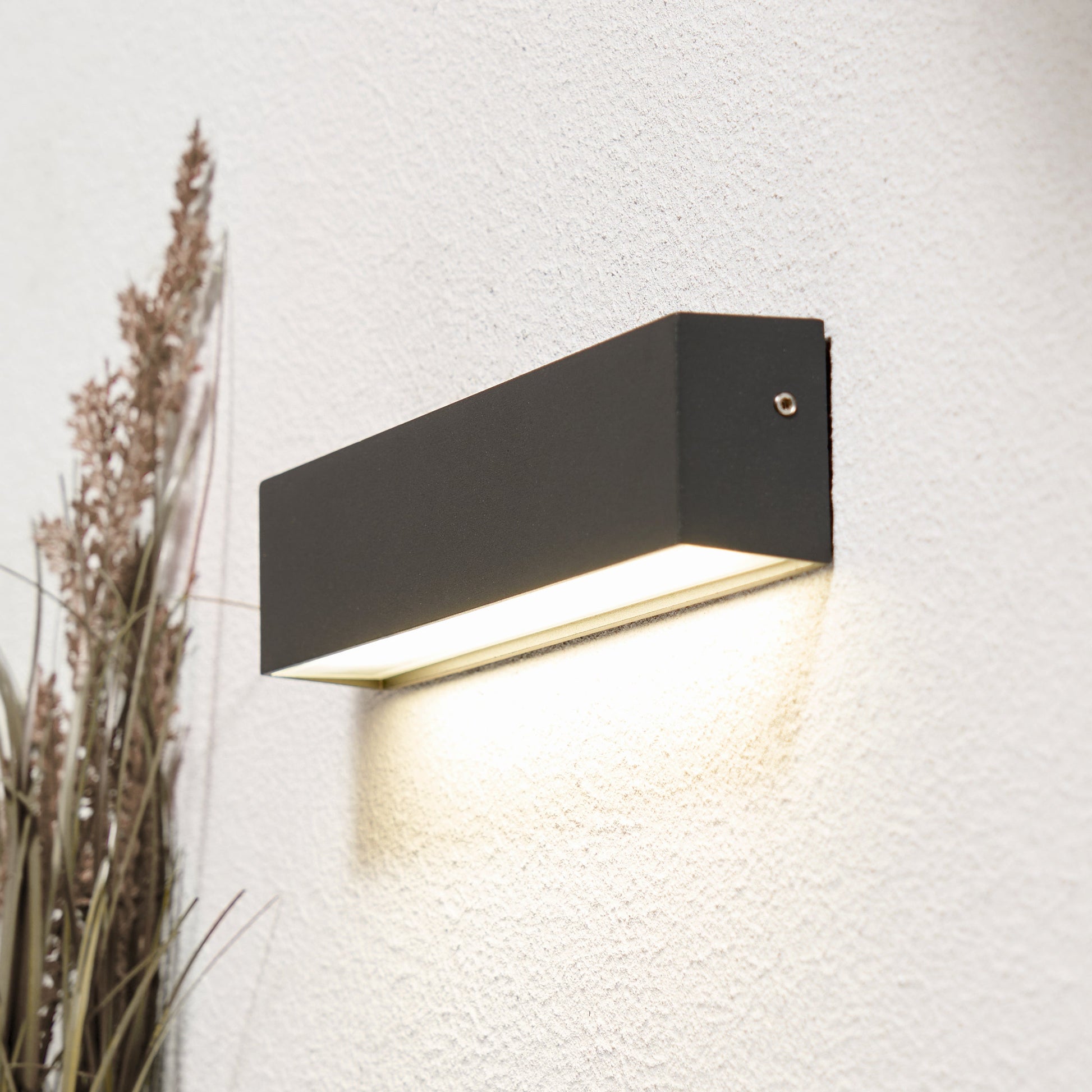 Modern black wall-mounted outdoor light fixture on a textured white wall.