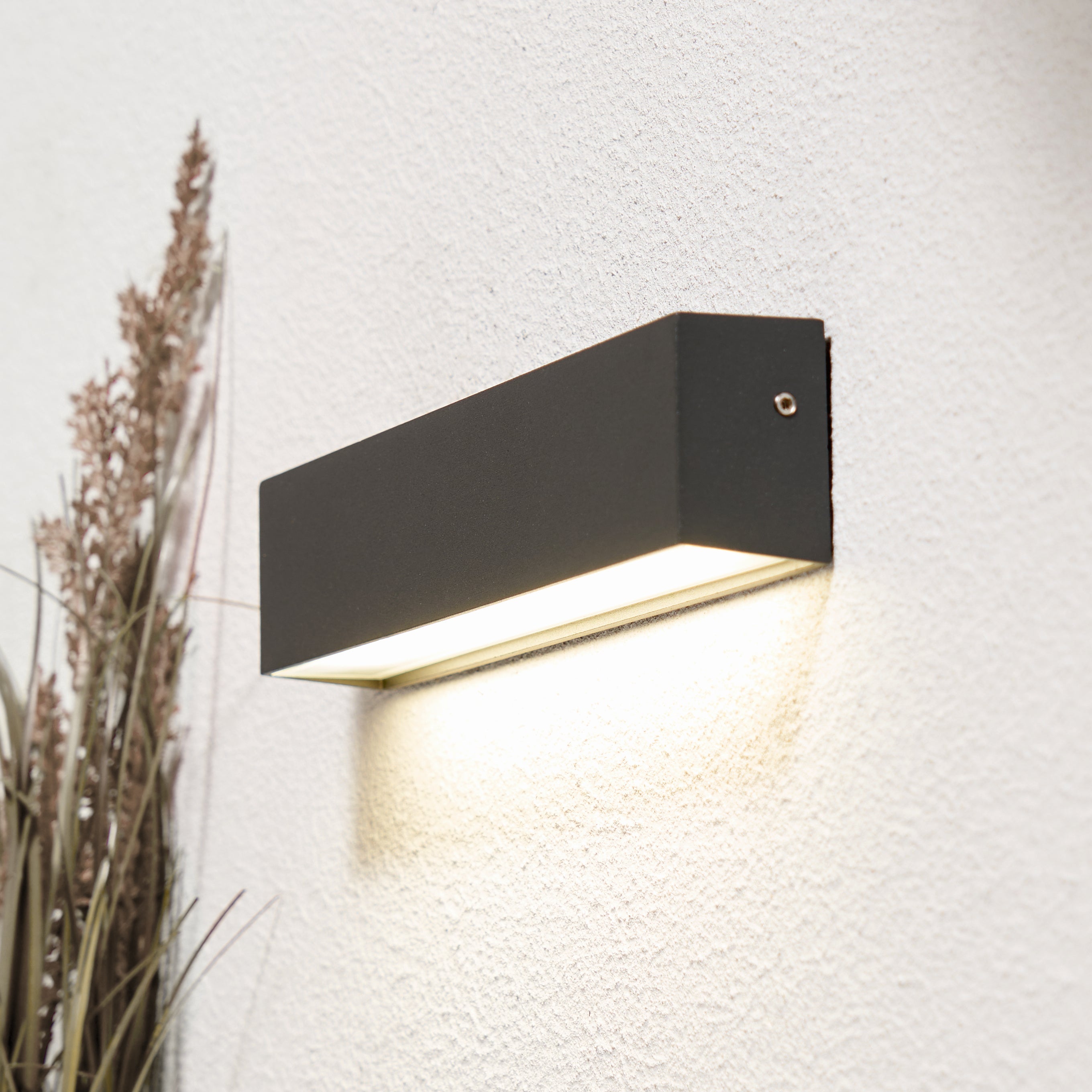 Modern black wall-mounted outdoor light fixture on a textured white wall.