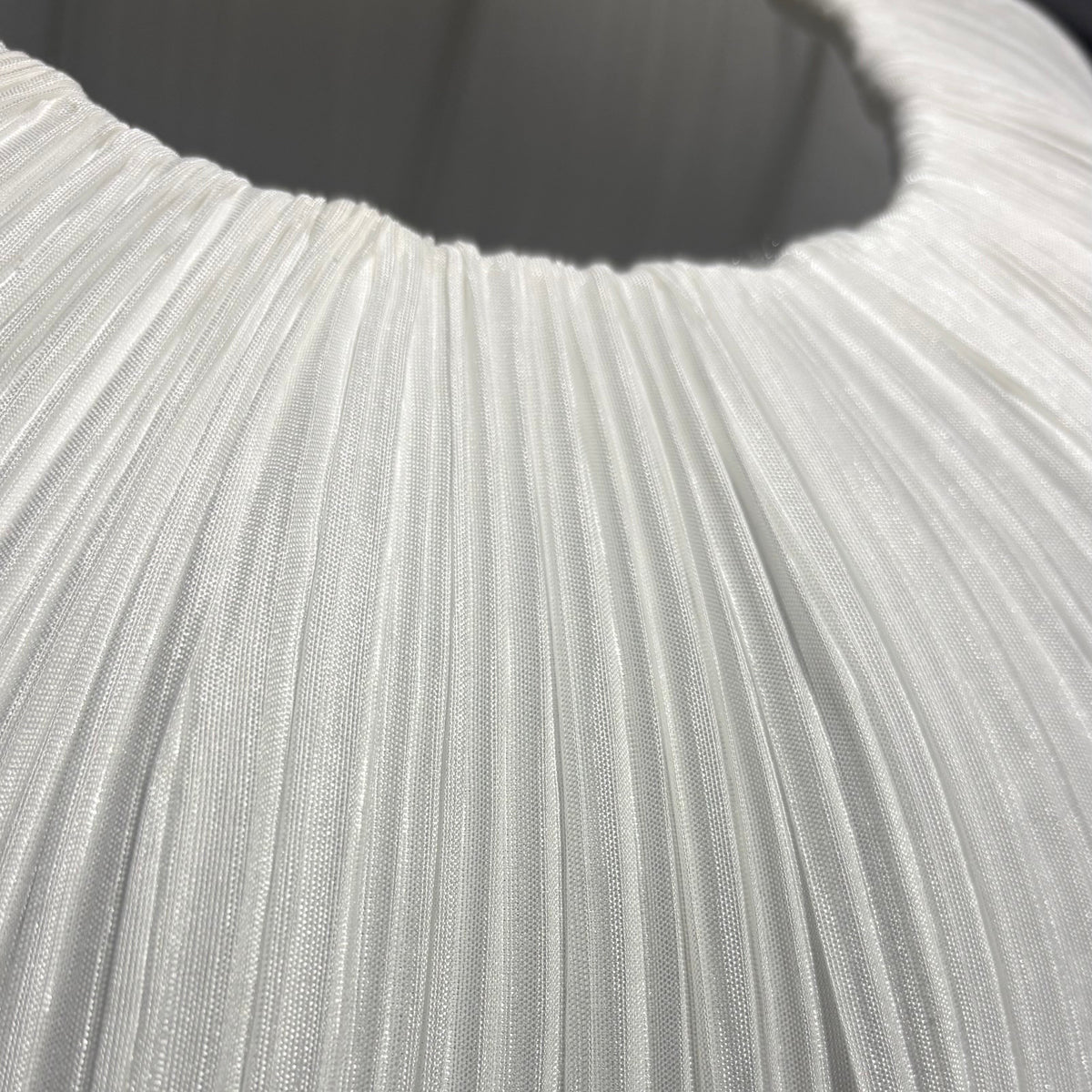 Close-up of a white pleated fabric surface with vertical folds and a curved opening at the top.