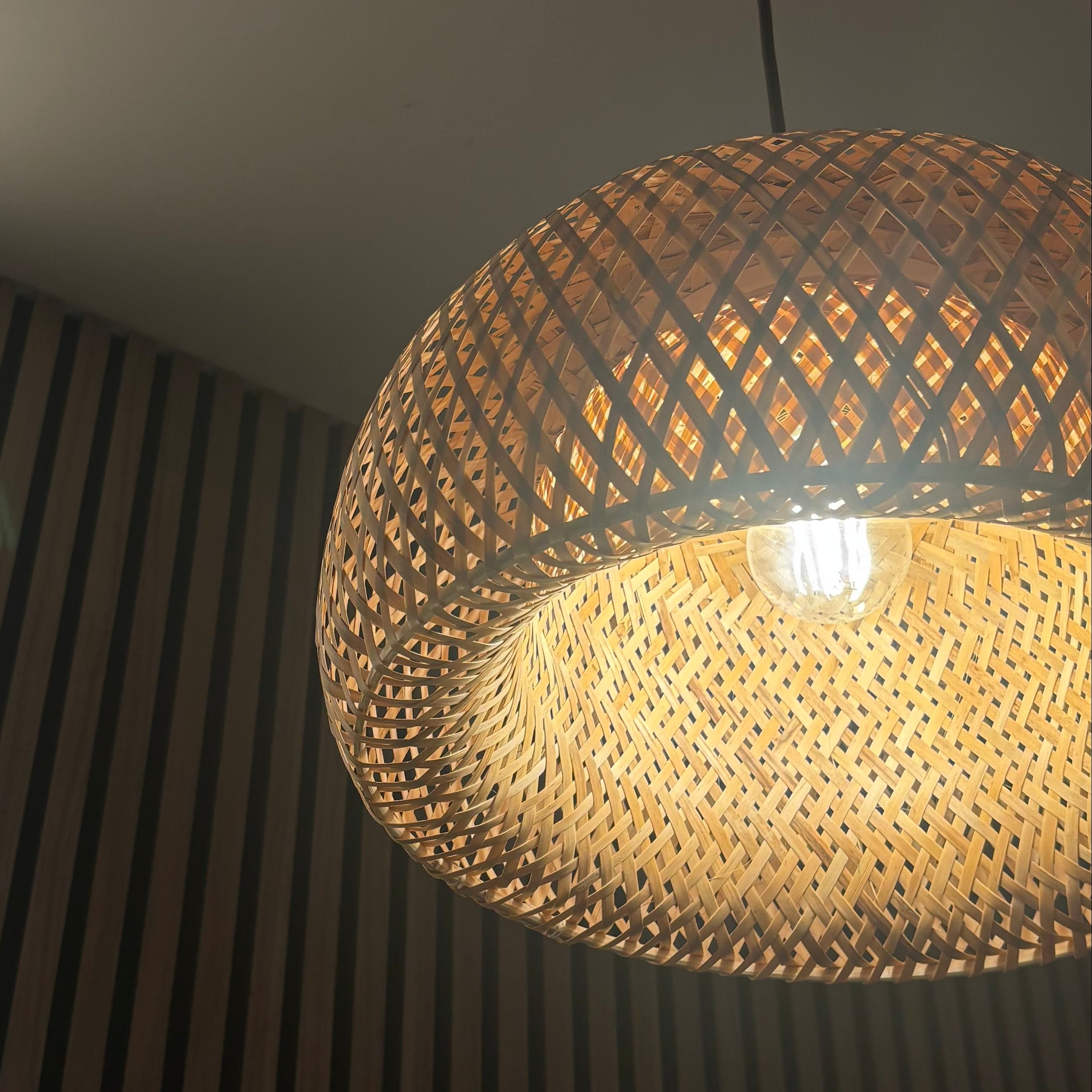 Woven pendant light hanging from a ceiling with a textured wall in the background