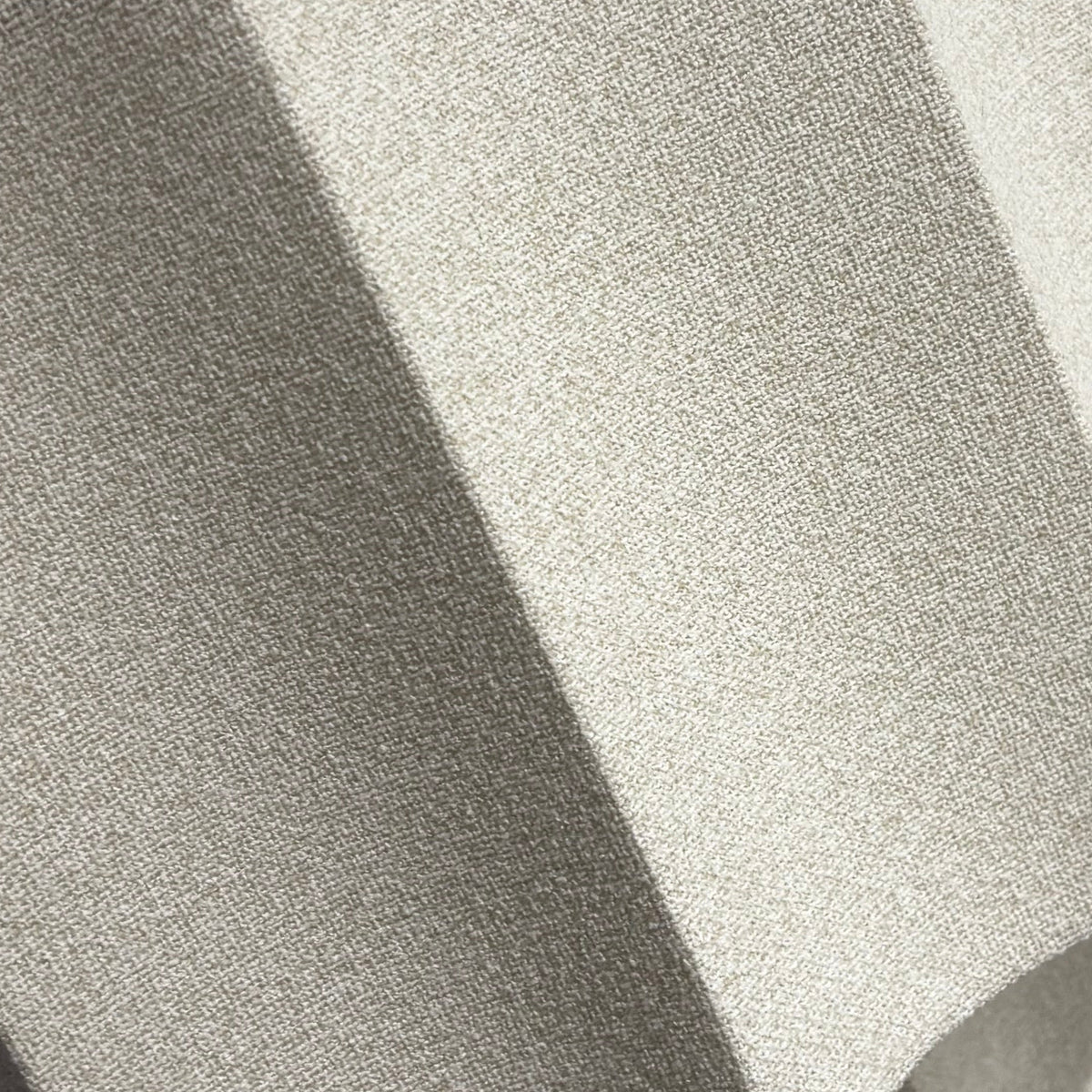 A close-up of a textured, light gray fabric or foam panel with a wavy, accordion-like pleated structure, held in place by a hand. The background shows a white wall with a blue geometric logo and a dark blue carpeted floor.