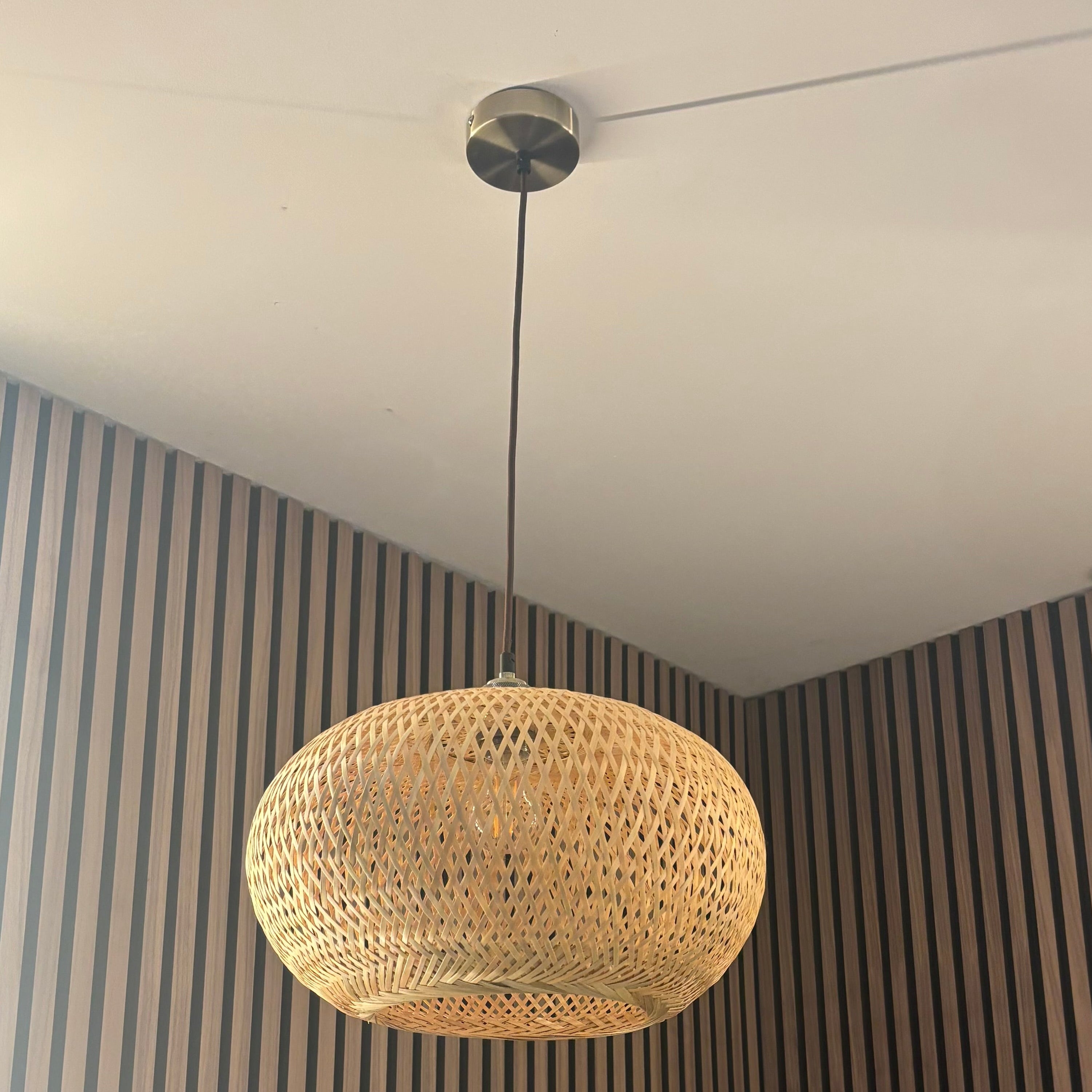 Woven pendant light hanging from a ceiling with striped walls in the background