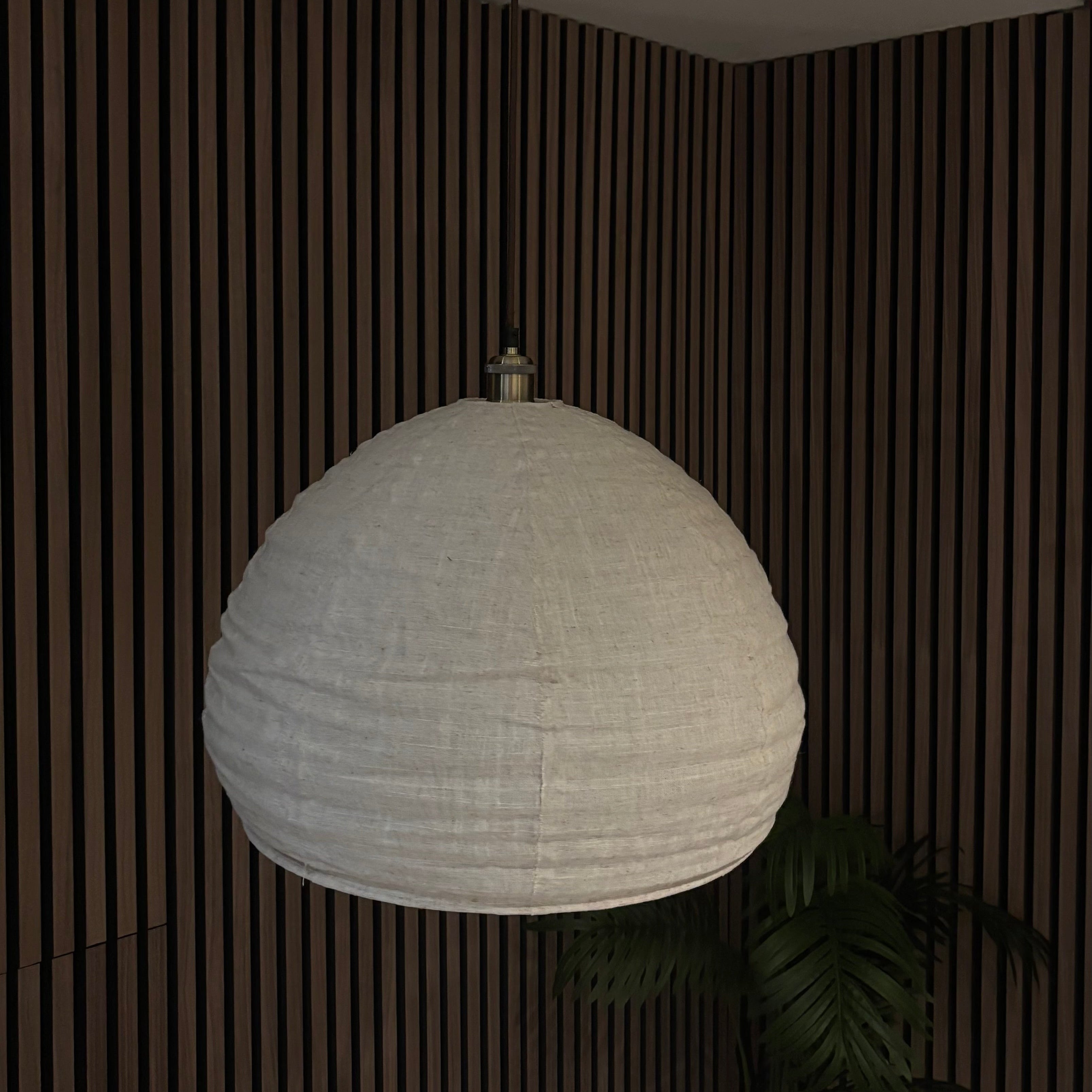 White pendant light hanging from a ceiling in a room with wooden paneling.