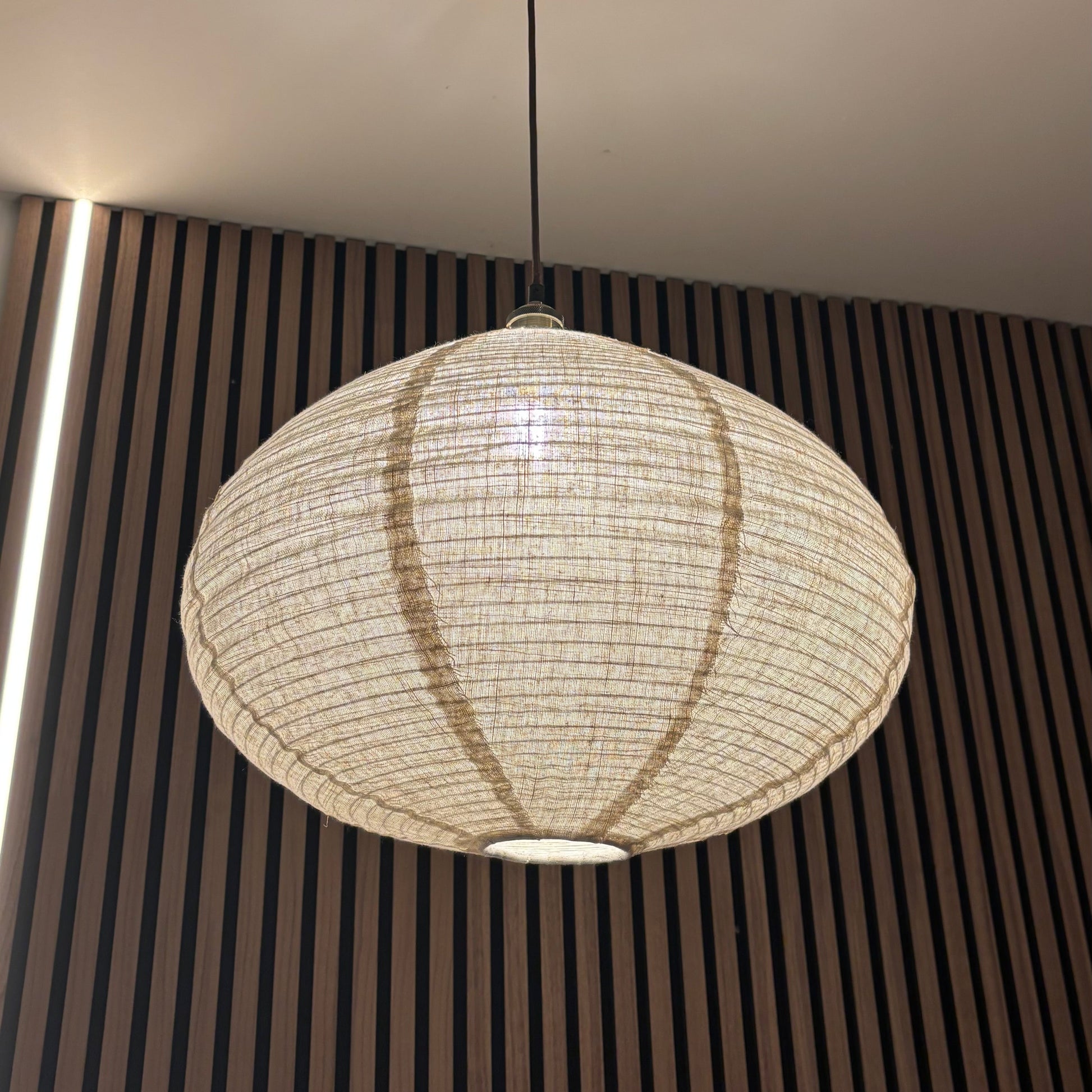 Round pendant light hanging from a ceiling with a striped wall in the background