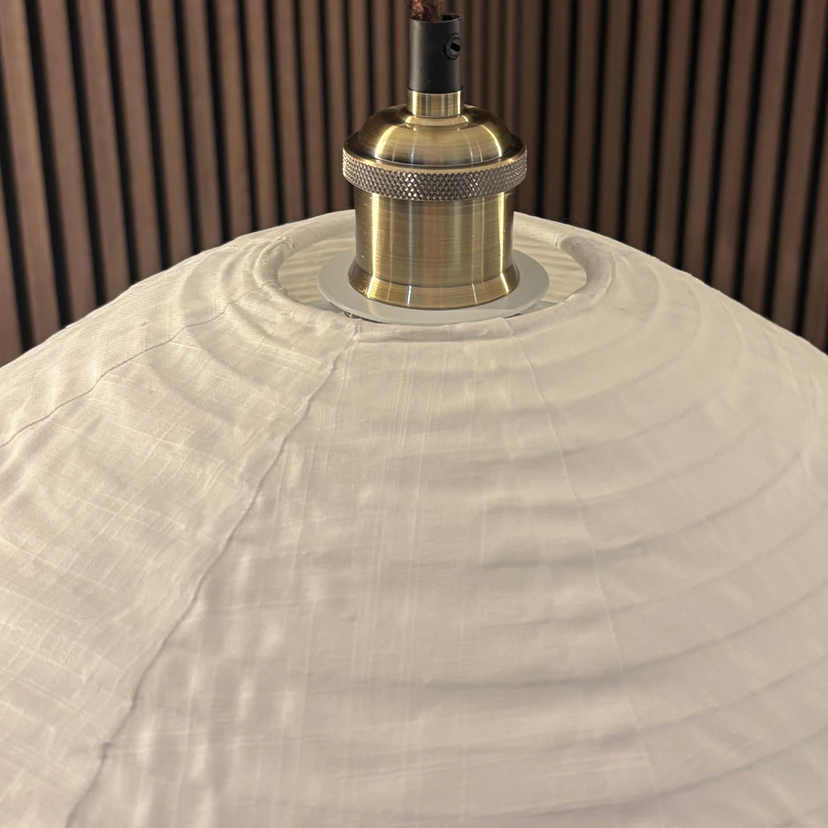 Close-up of a lampshade with a visible light bulb against a wooden panel background
