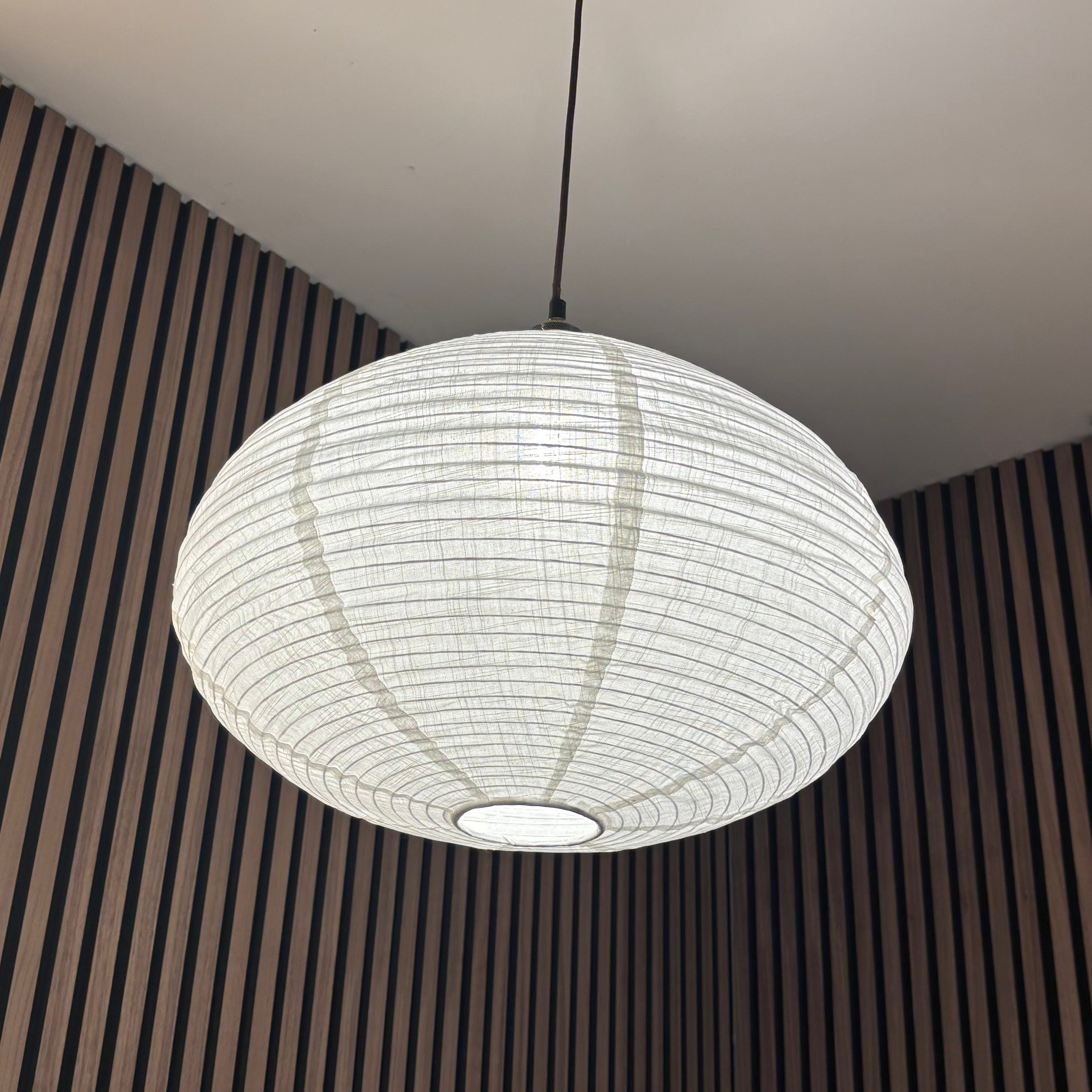 Round pendant light hanging from the ceiling with a striped wall in the background