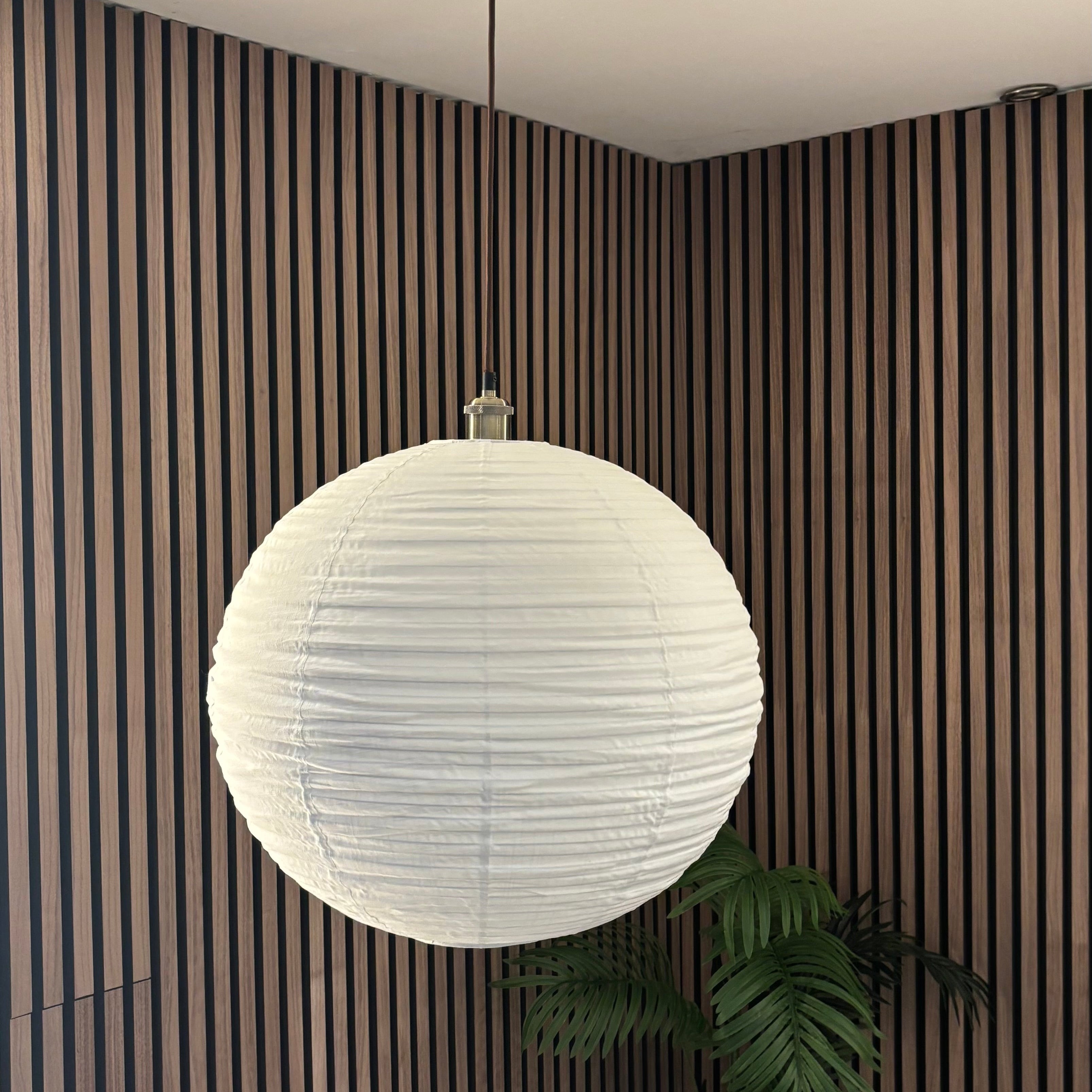 White spherical pendant light hanging in a room with striped walls and a plant.