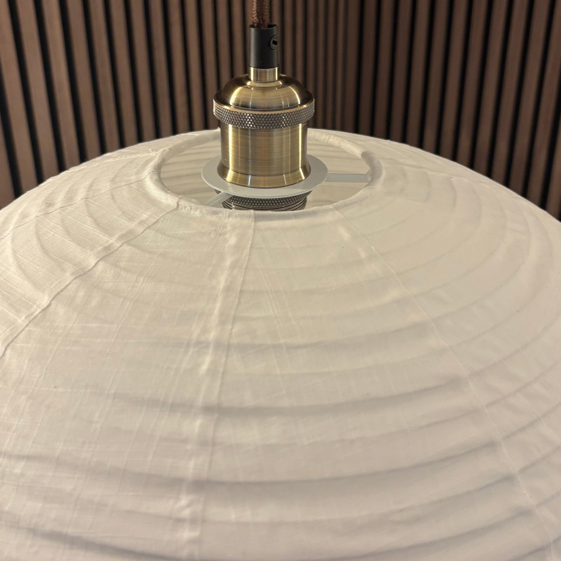 Close-up of a lampshade with a metallic fitting against a wooden panel background