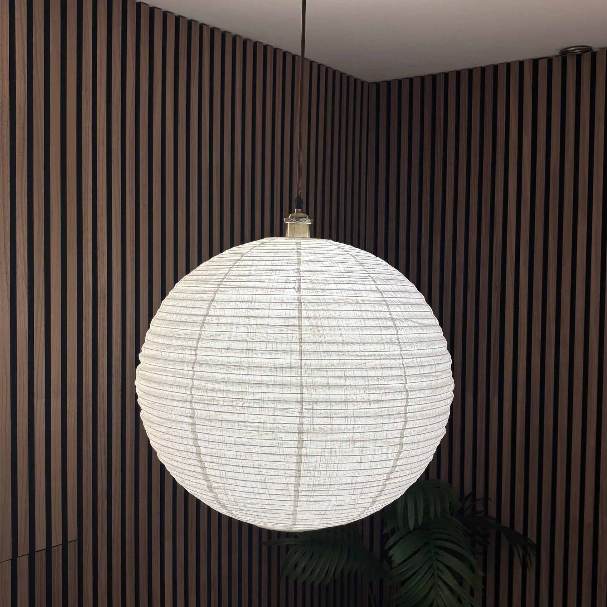 White spherical pendant light hanging in a room with striped walls and a plant.