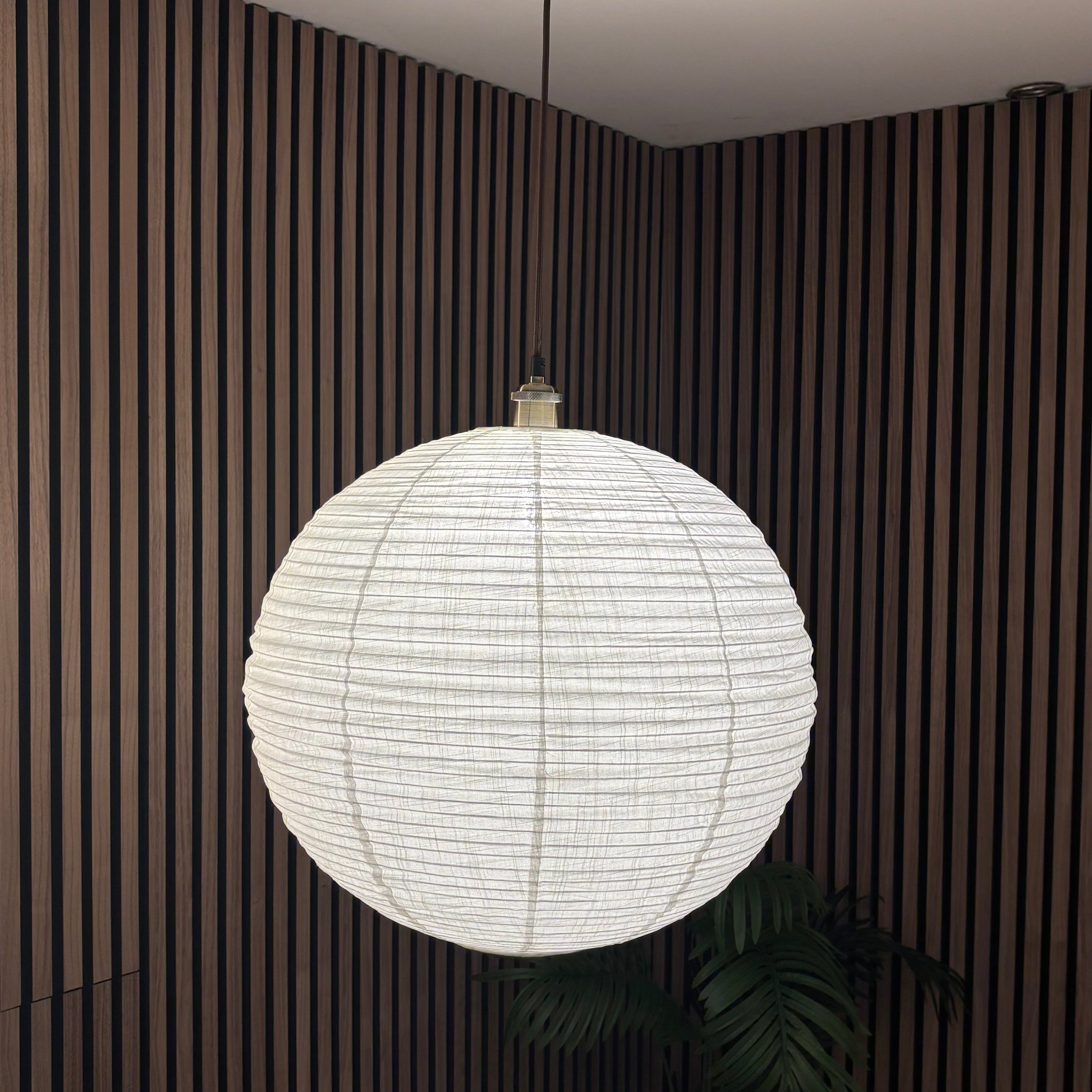 White spherical pendant light hanging in a room with striped walls and a plant.