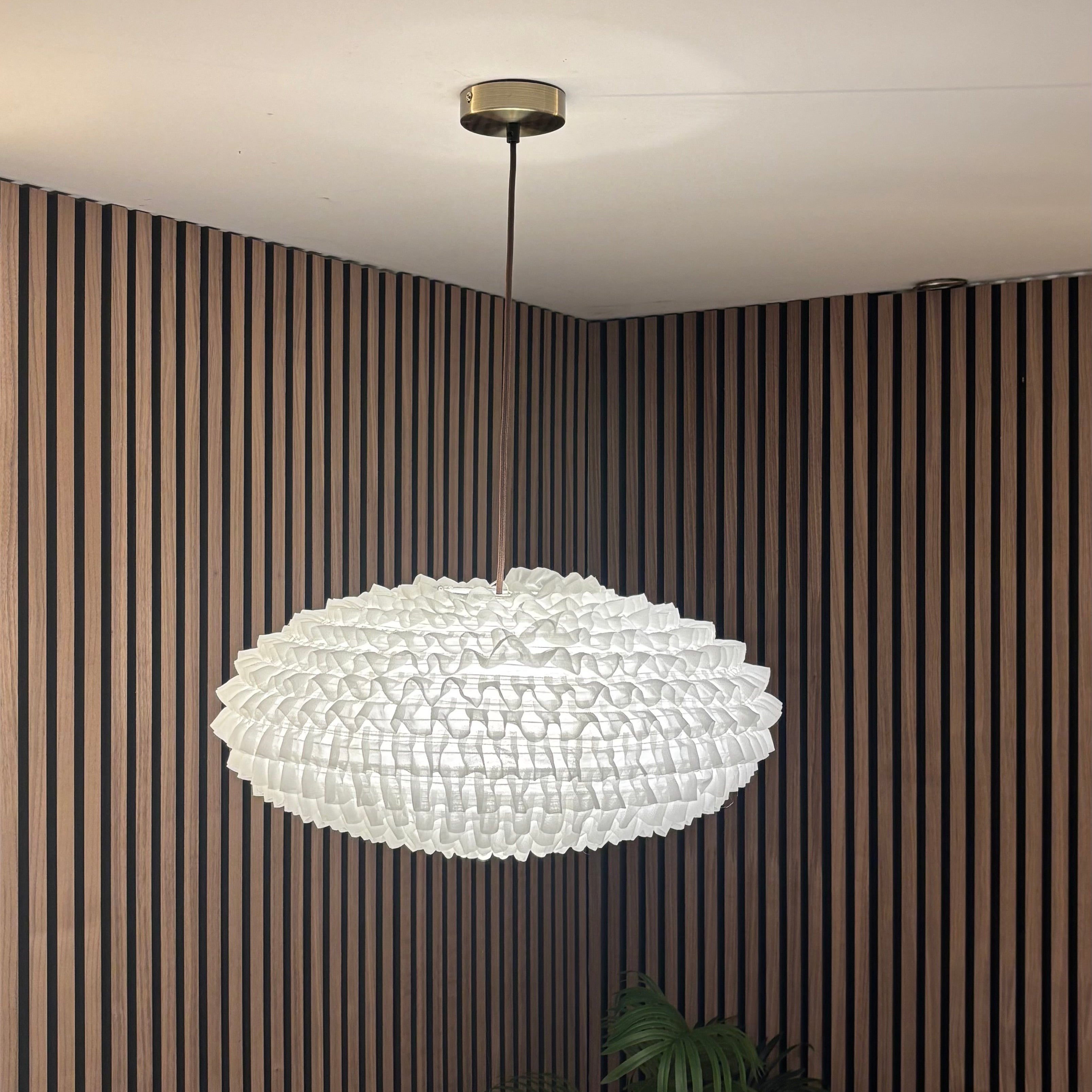 Modern chandelier hanging in a room with striped walls and a plant.
