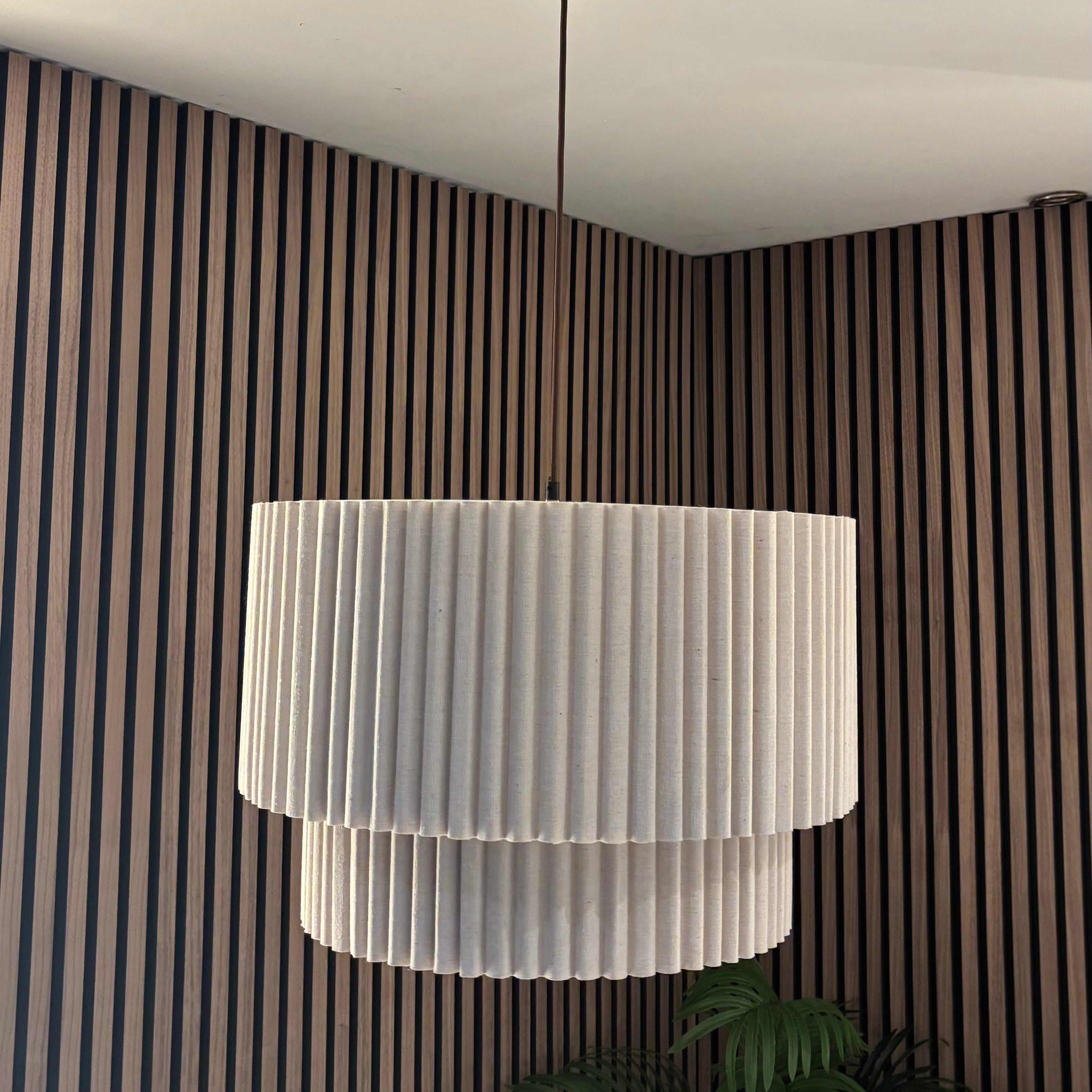 White pleated lampshade hanging from a ceiling in a room with striped walls.