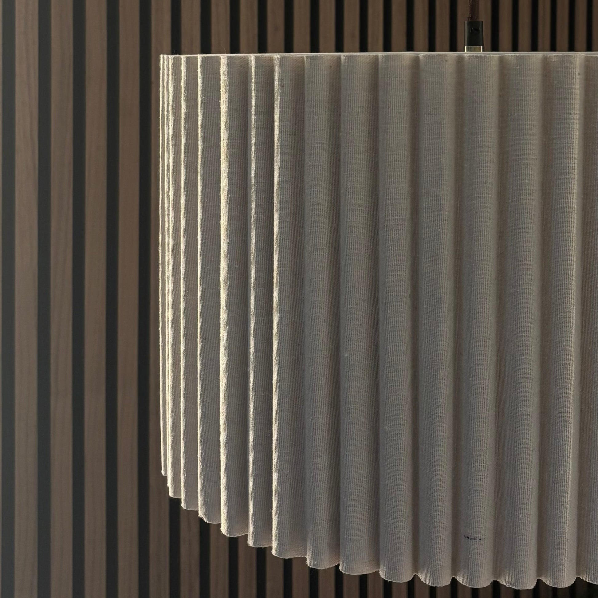 Modern pendant light fixture hanging from a ceiling with a striped wall in the background