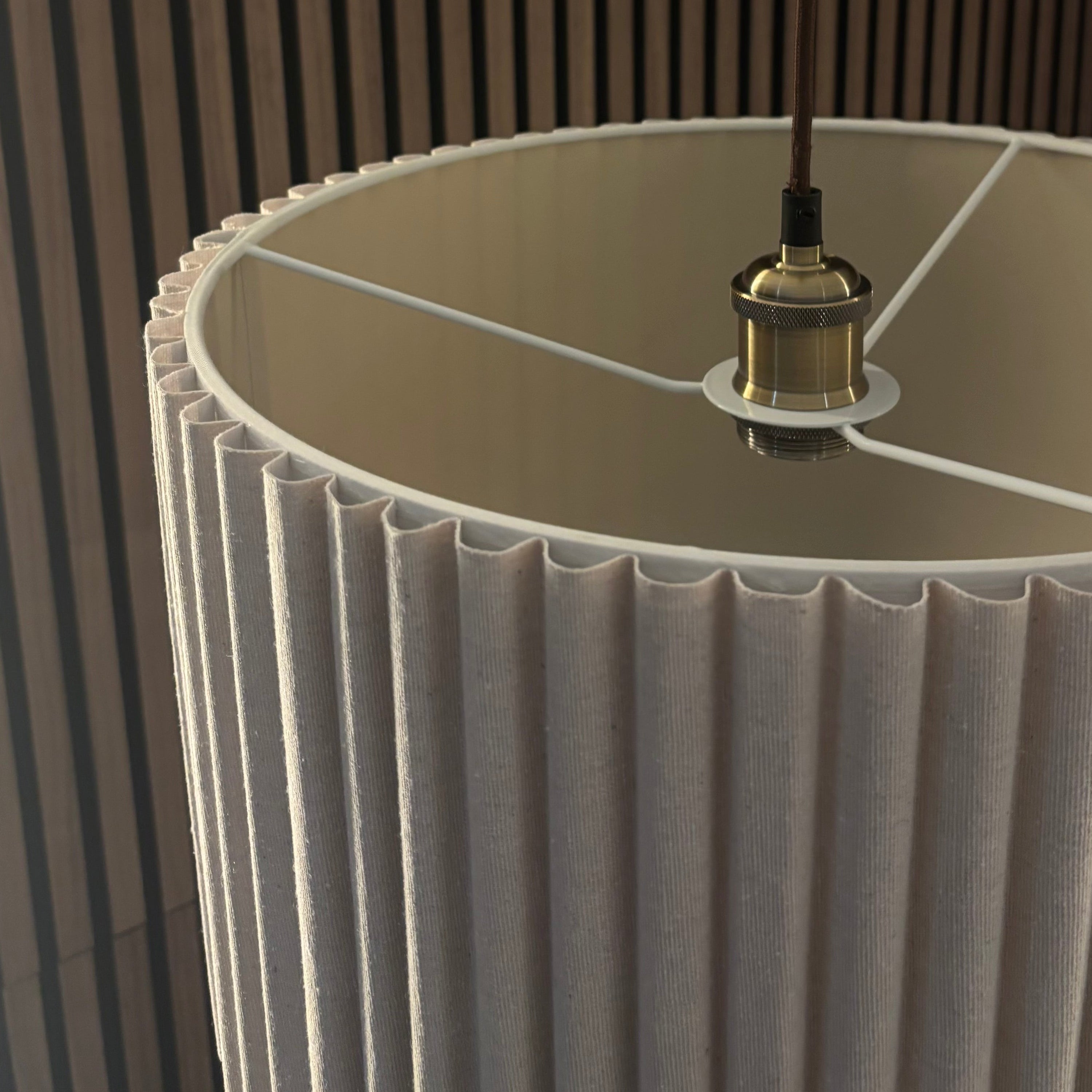 Close-up of a pleated lampshade with a visible light bulb against a wooden panel background