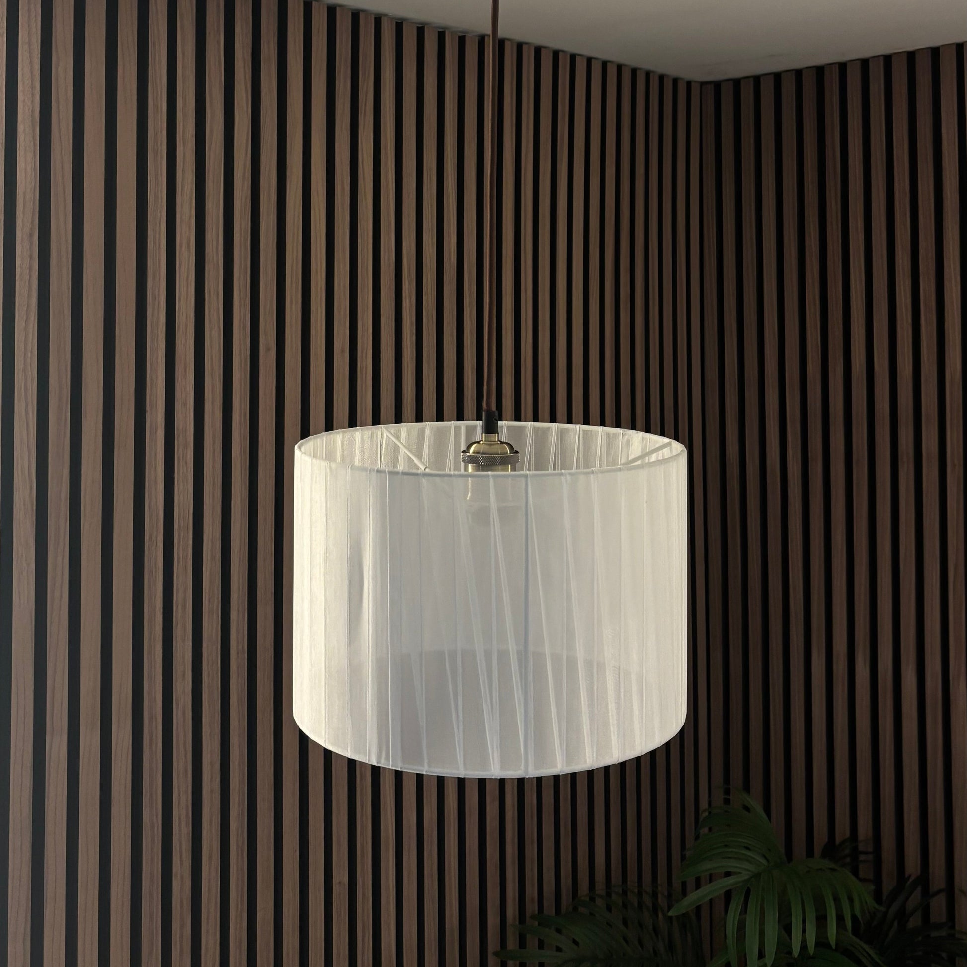 White pendant light hanging from a ceiling with striped walls and a plant in the corner.