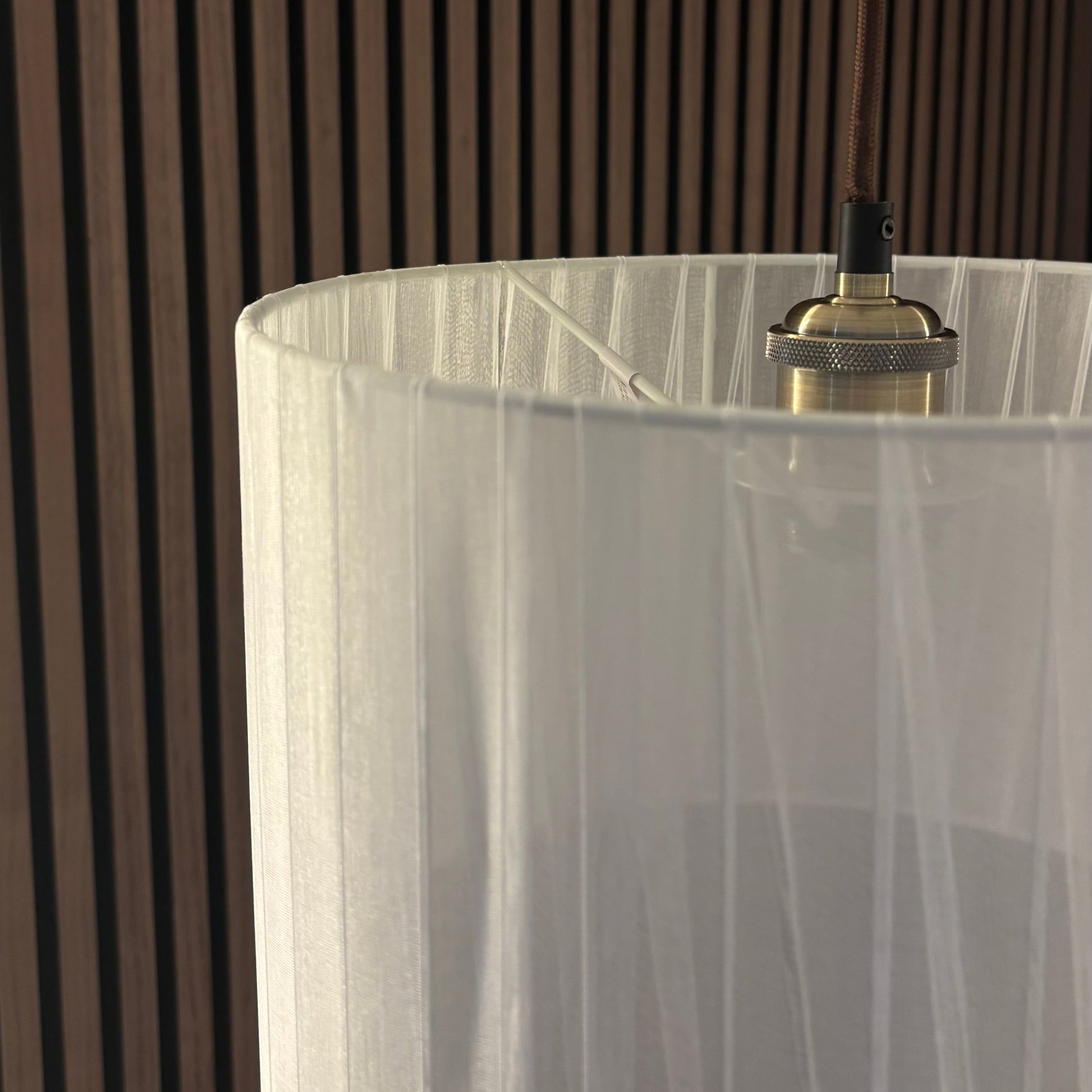 Close-up of a modern light fixture with a white shade against a wooden slat background