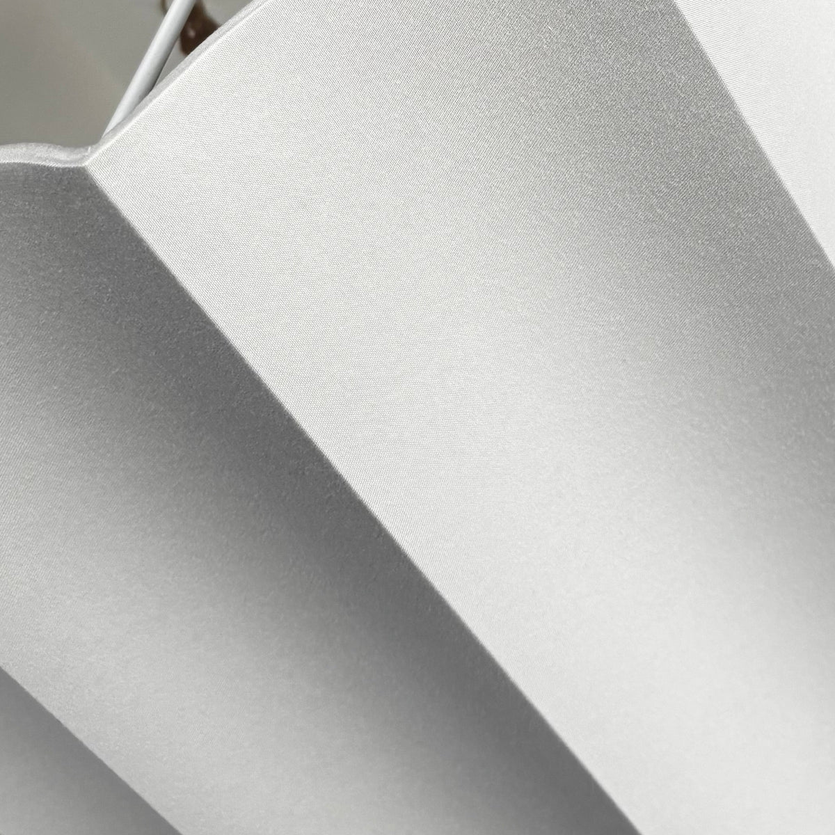 A pale grey pleated fabric or mesh lampshade being held by a person's hand, with a dark warehouse or storage area in the background.