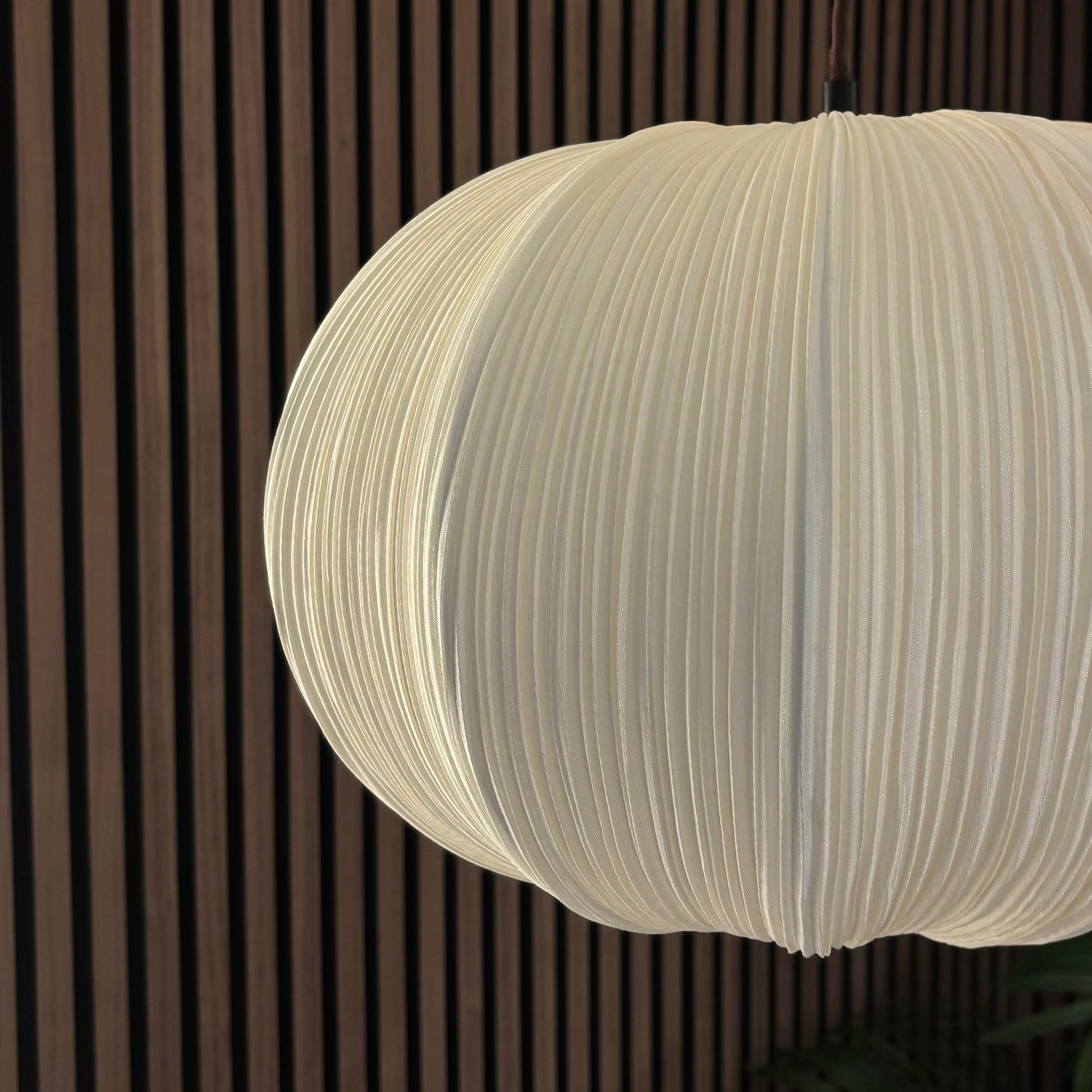 White pendant light hanging against a dark wooden panel wall.