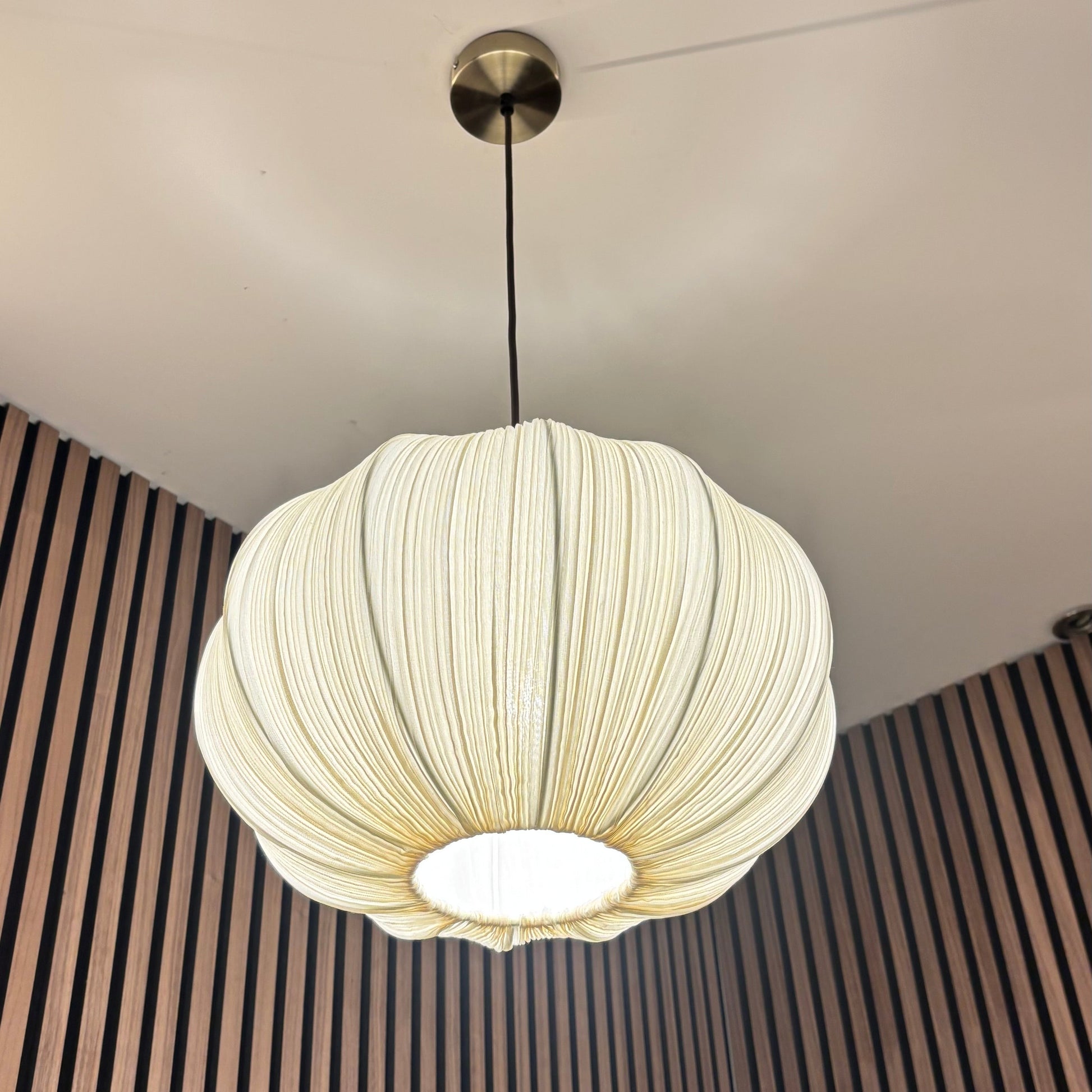 White pendant light hanging from a ceiling with a striped wall in the background