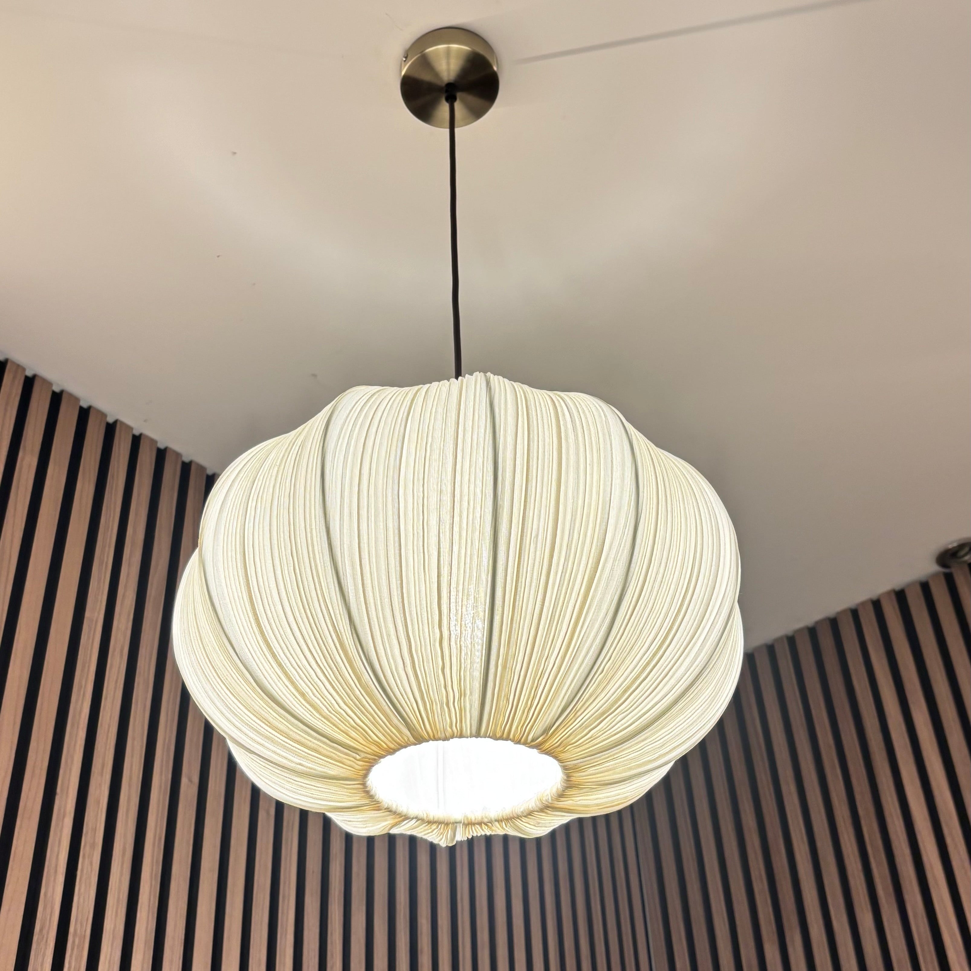 White pendant light hanging from a ceiling with a striped wall in the background