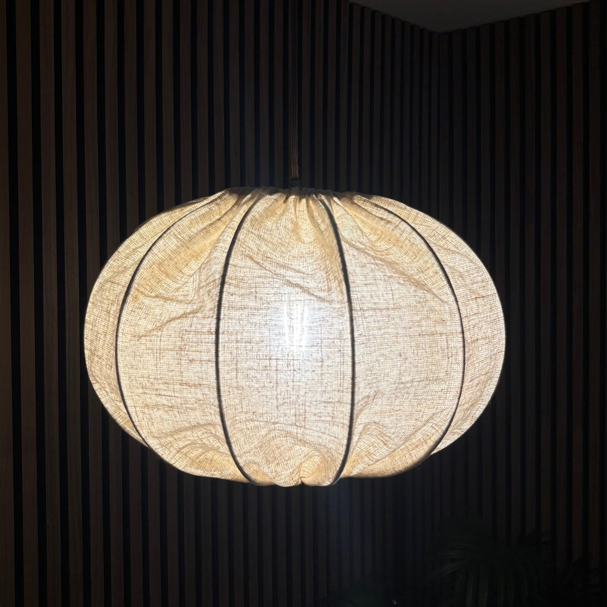 Round woven pendant light hanging against a dark background