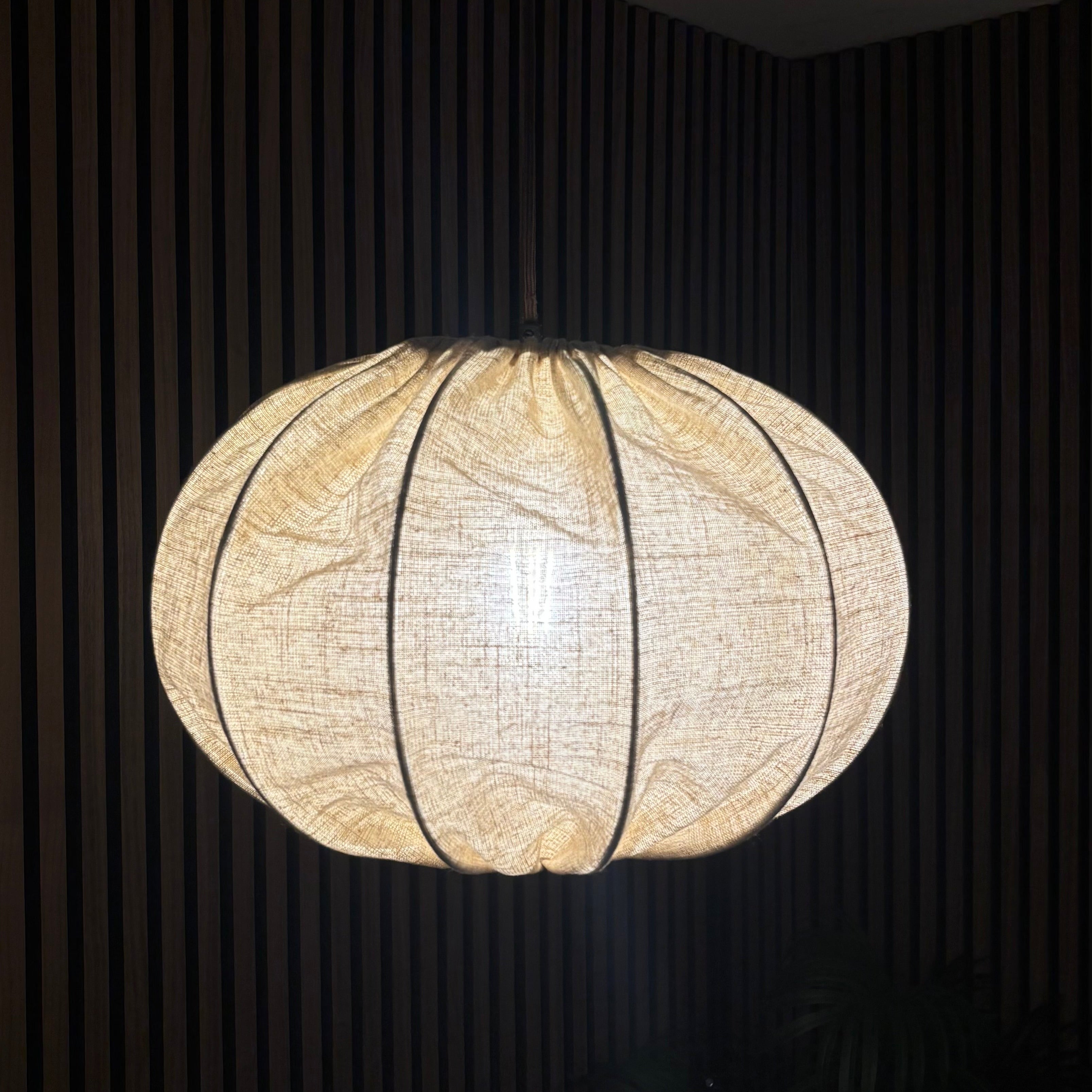 Round woven pendant light hanging against a dark background